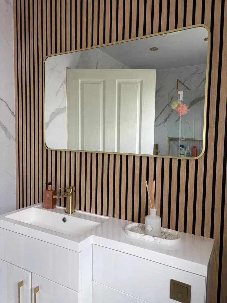 Contemporary bathroom vanity with gold-framed mirror, wood-slat feature wall, and polished white surfaces after deep cleaning