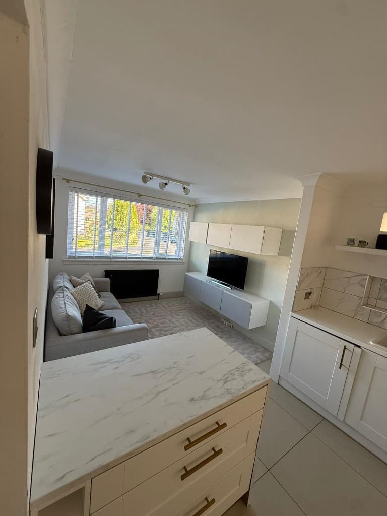 Open-plan kitchen and living area with marble countertops, gold hardware, and a styled grey sofa after turnover cleaning